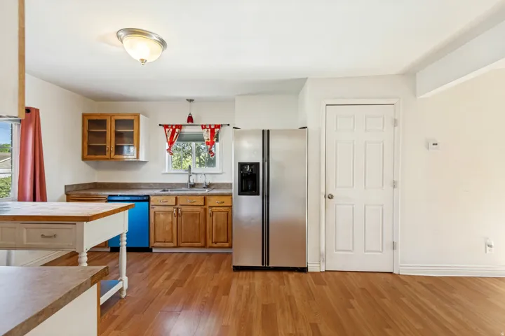 Bright kitchen space featuring wood-finish flooring, a stainless steel refrigerator, and ample cabinetry