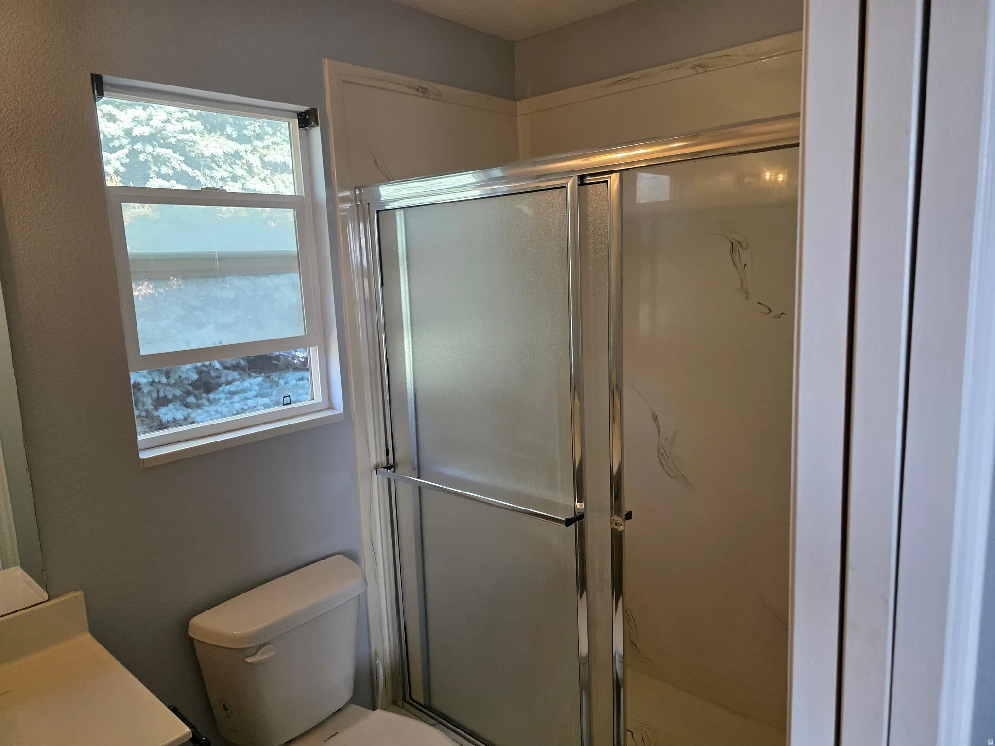 Full bathroom featuring a shower with sliding glass doors, a window with exterior visibility, and a commode