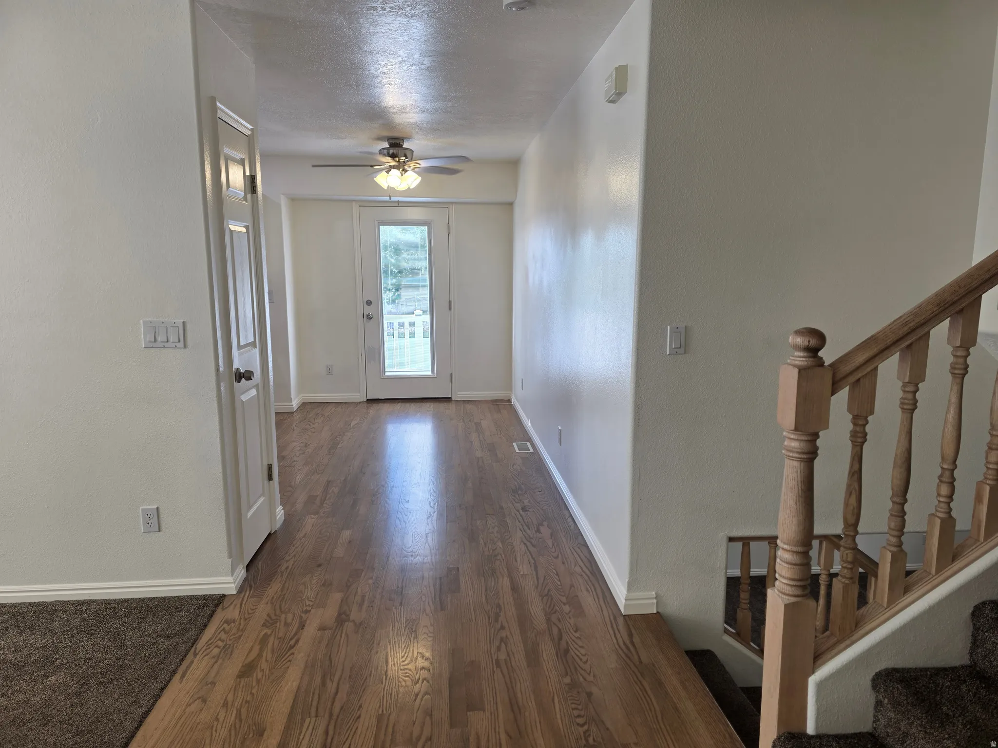 Hallway featuring wood-finish flooring extending into a room with a ceiling fan light fixture, white interior doors, and a glass-paneled exterior door