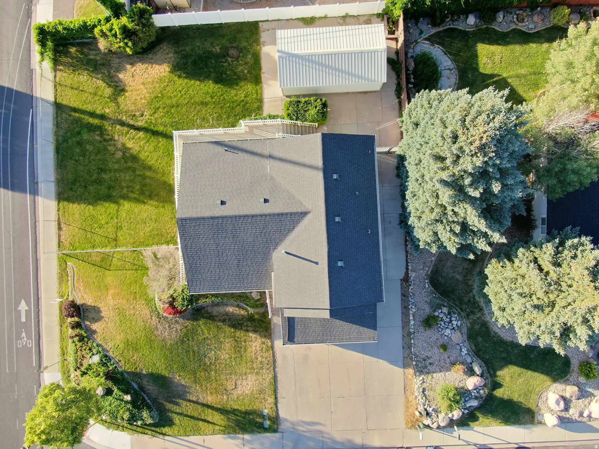 Expansive property featuring a dark-shingled roof, a concrete driveway, and mature landscaping