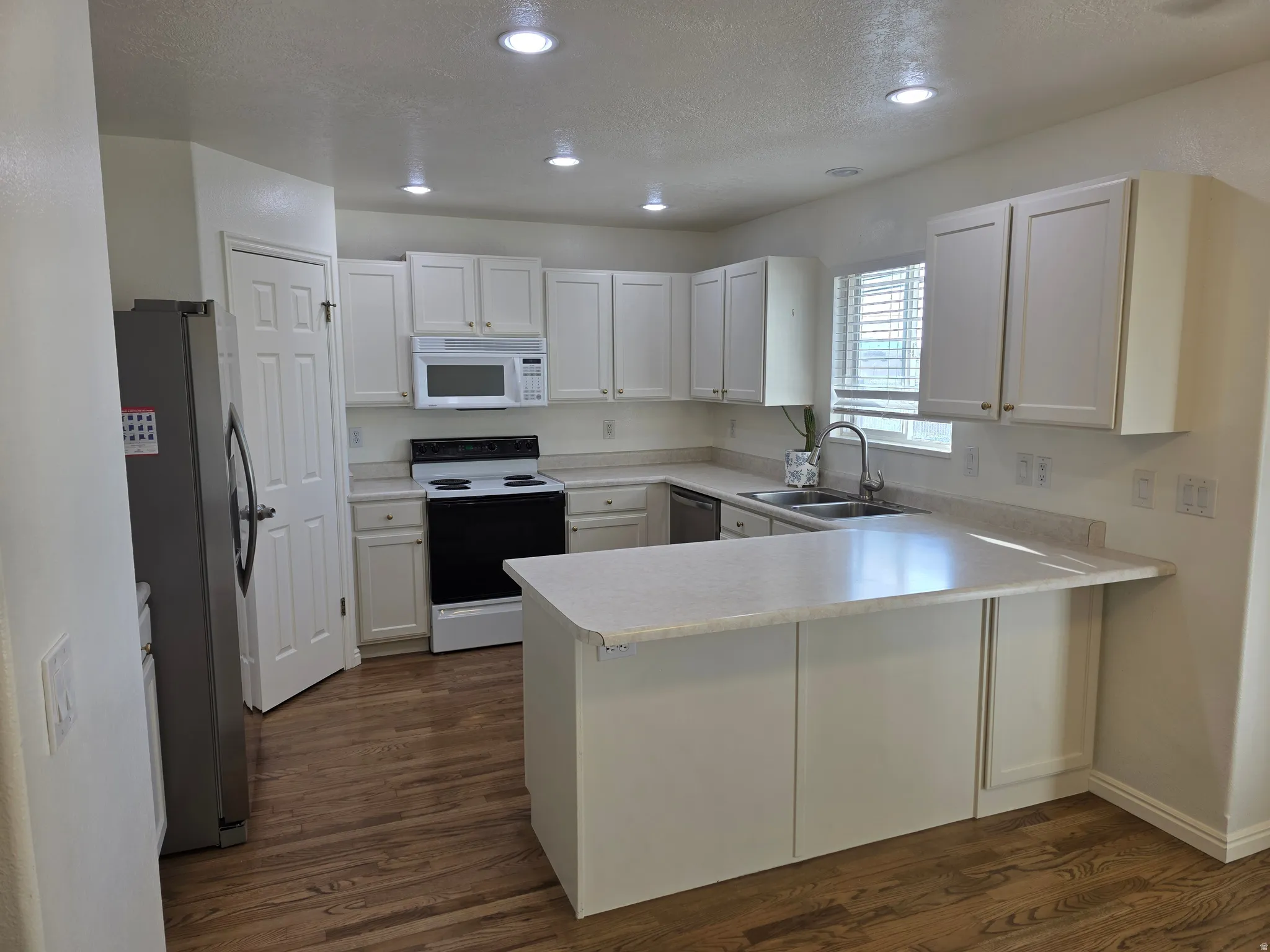 Kitchen featuring white cabinetry, light-toned countertops, a stainless steel refrigerator, a black electric range with an overhead microwave, and recessed lighting