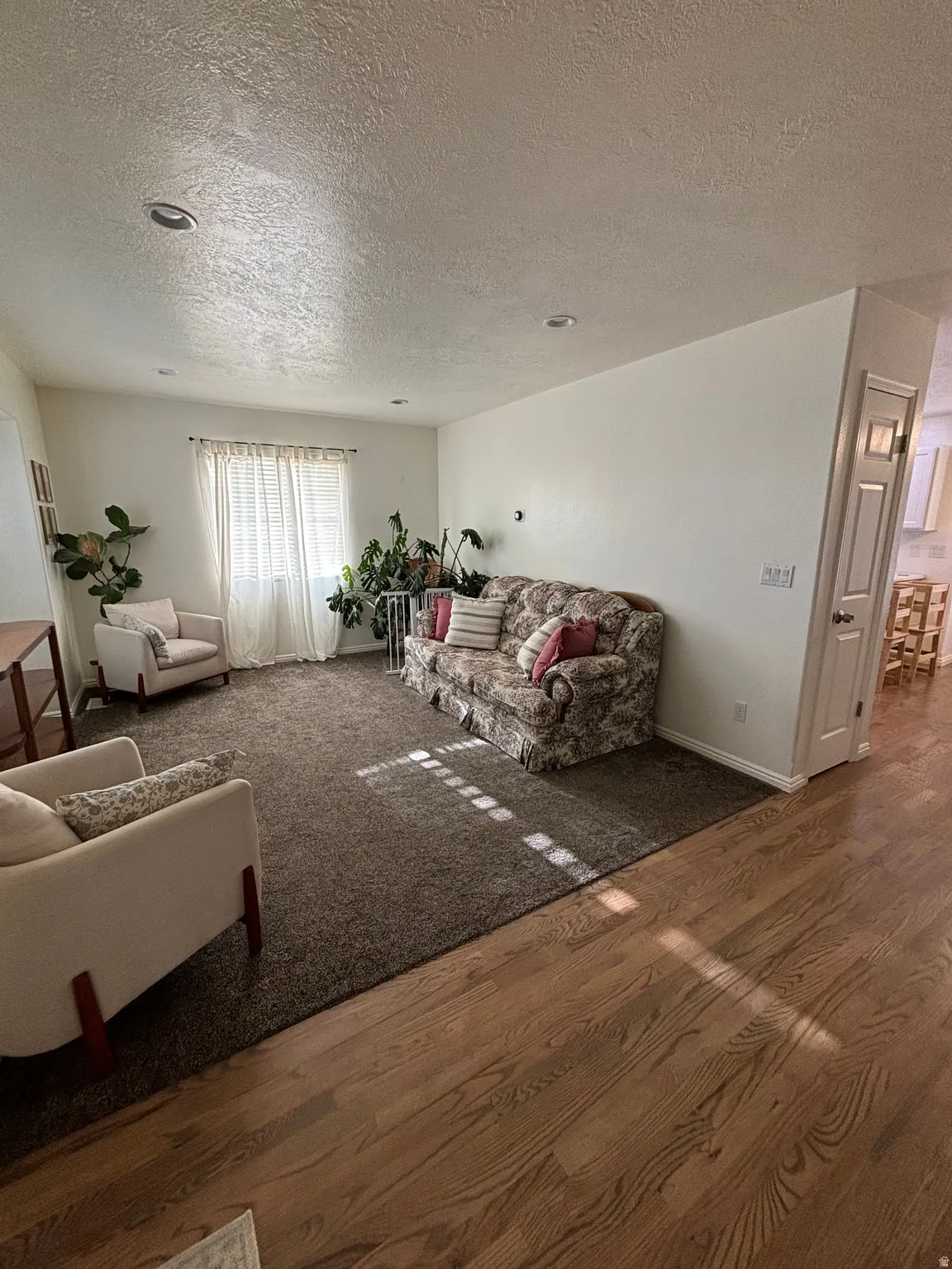 Recessed lighting illuminates this living space featuring a window with blinds, brown carpet, and wood-finish flooring