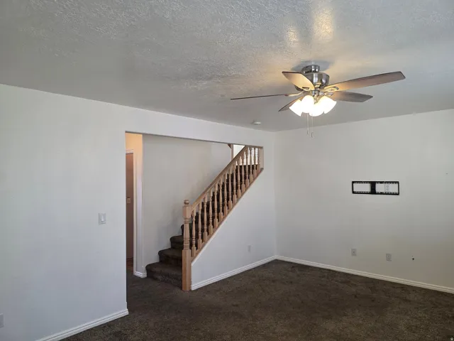Interior space featuring a carpeted staircase with wood banister, wall-to-wall carpeting, white painted walls, and a ceiling fan with light fixture