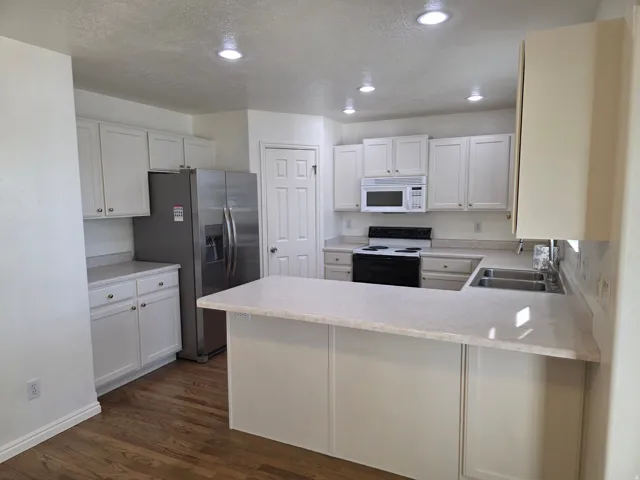 Kitchen featuring wood-finish flooring, white cabinetry, stainless steel refrigerator, white microwave, and recessed lighting