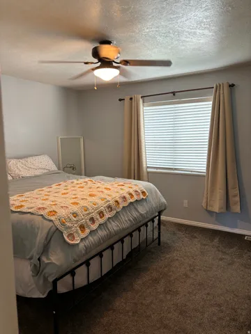 Bedroom featuring a ceiling fan with integrated lighting, a window with horizontal blinds, and neutral carpet flooring