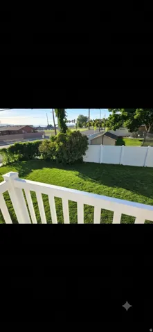 Expansive green lawn with a white vinyl fence and mature shrubbery