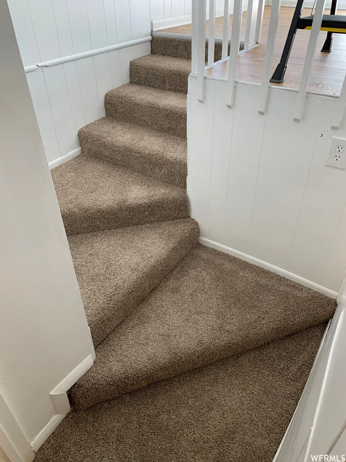 Carpeted staircase featuring a neutral-toned plush pile, white vertical paneling, and white balusters
