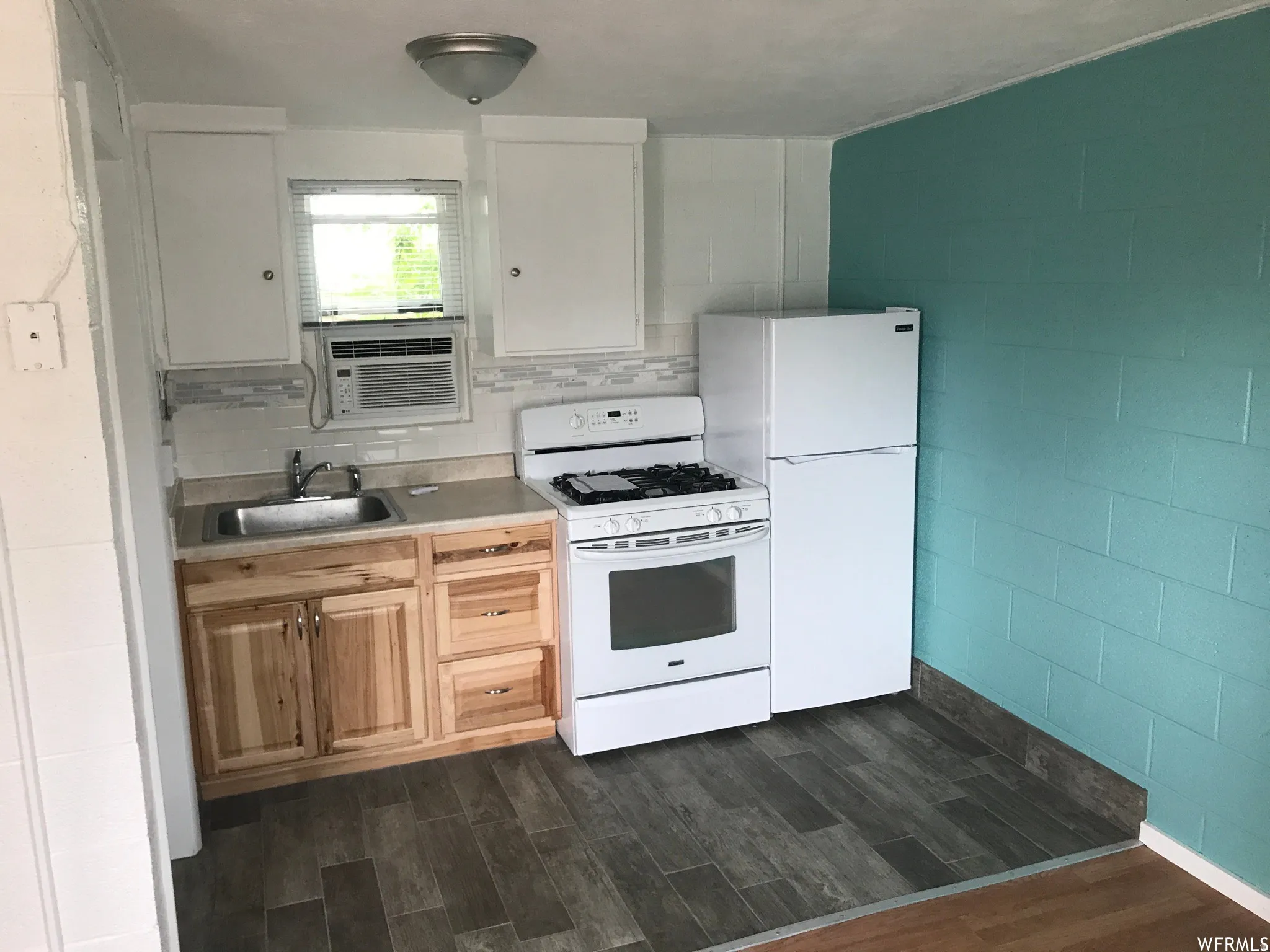 Kitchen space featuring wood-finish flooring, light wood cabinetry, white upper cabinets, a white gas range, and a white refrigerator
