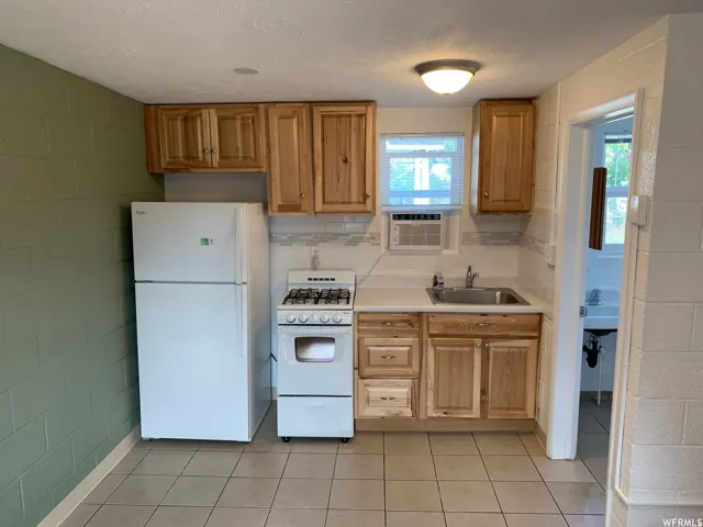 Compact kitchen featuring natural wood cabinetry, a stainless steel sink, and white appliances
