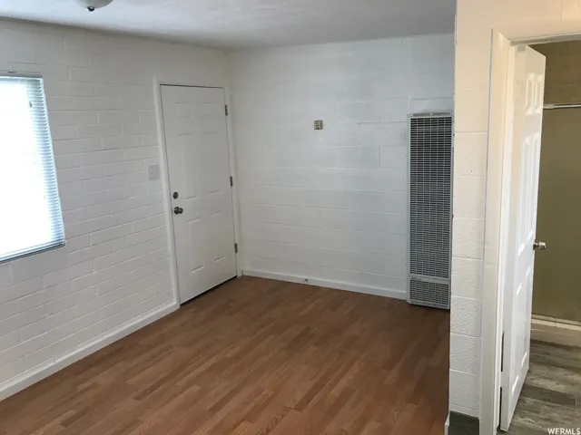 Interior space featuring white painted brick walls, wood-finish flooring, and a wall-mounted heating unit