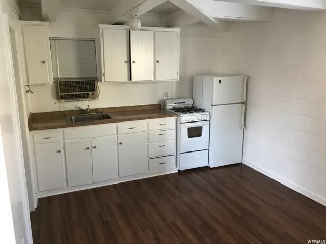 Kitchen area featuring wood-finish flooring, white cabinetry, integrated sink, gas range, and refrigerator