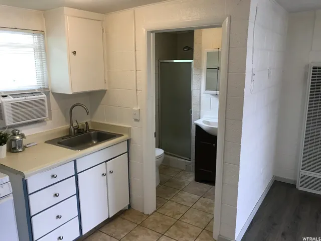Compact kitchen area featuring a stainless steel sink, white cabinetry with silver hardware, and a window with blinds
