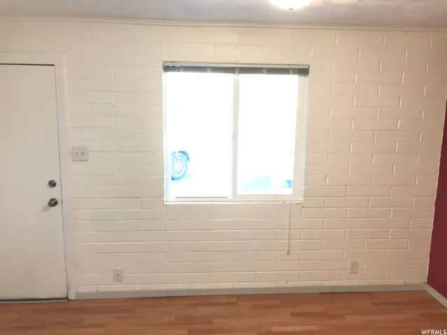 White painted brick wall with a double-pane window, wood-finish flooring, and white trim