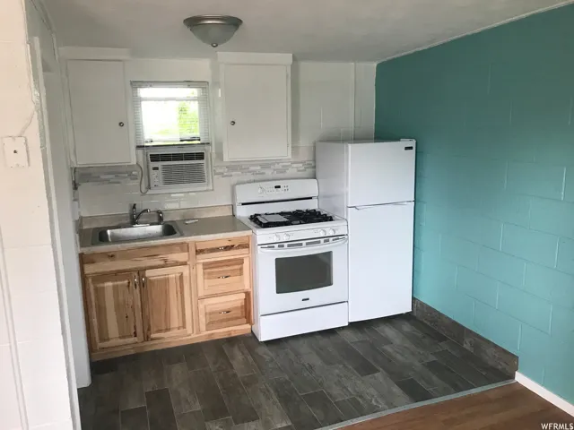 Kitchen space featuring wood-finish flooring, light wood cabinetry, white upper cabinets, a white gas range, and a white refrigerator
