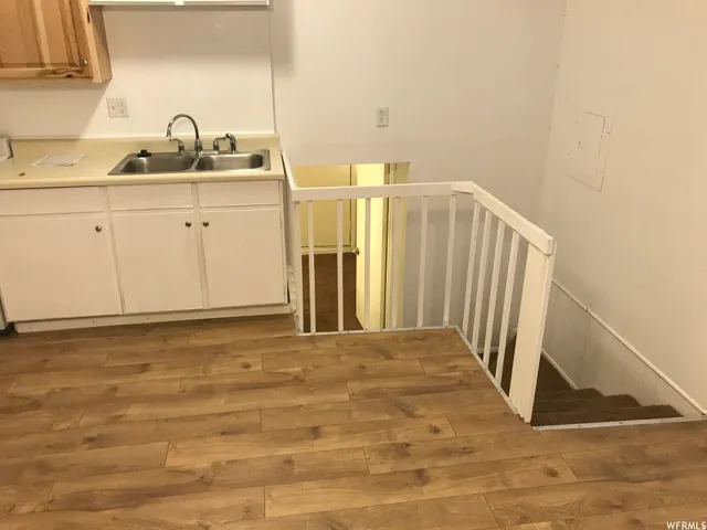 Kitchen area featuring wood-finish flooring, white cabinetry, a double basin stainless steel sink, and a staircase with a white railing