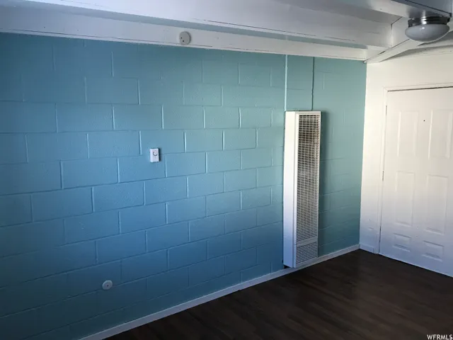 Block wall with light blue finish, wood-finish flooring, white door, wall-mounted heater, and ceiling-mounted light fixture