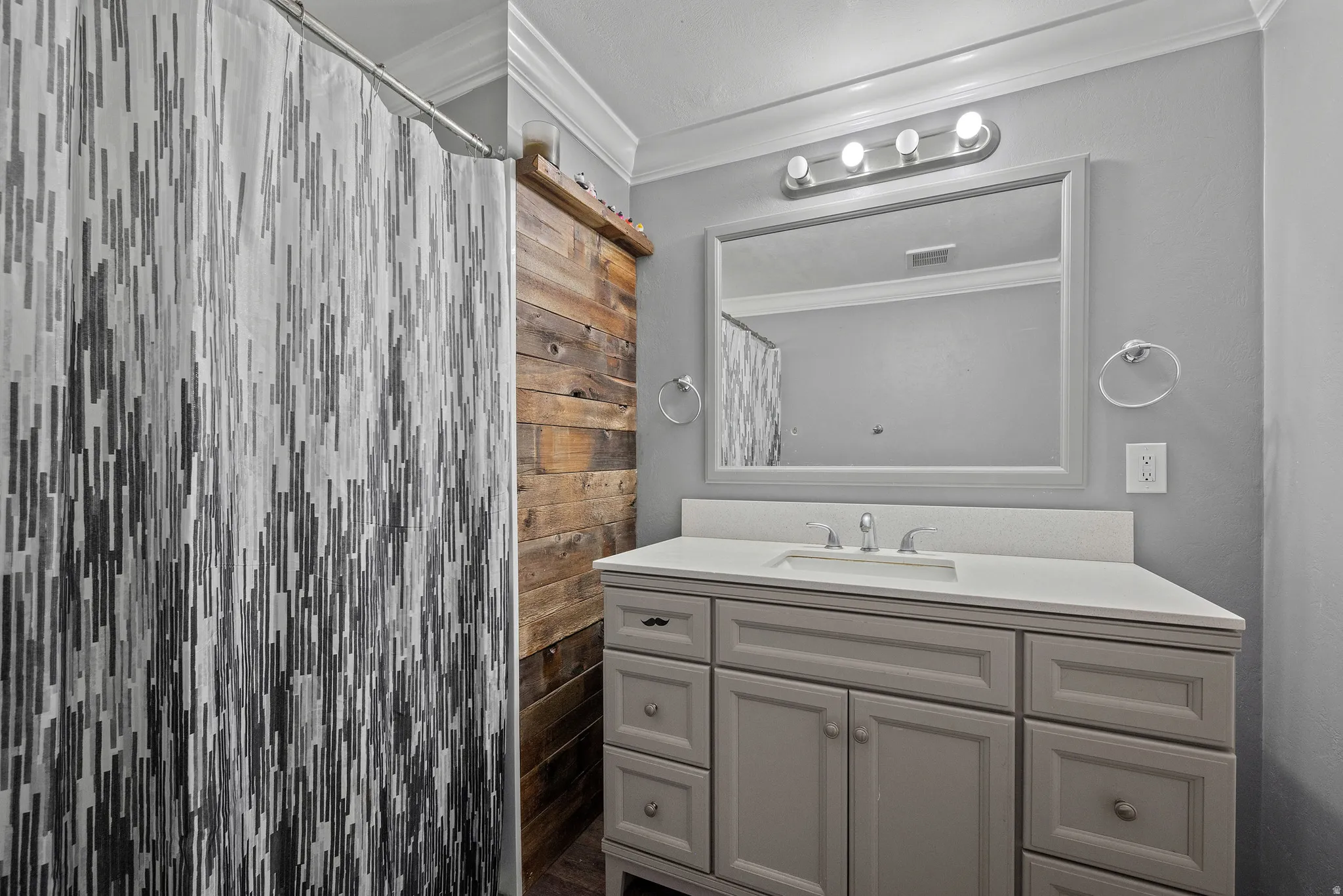 Bathroom featuring a single vanity with a white countertop and undermount sink, framed mirror, and a four-bulb vanity light fixture
