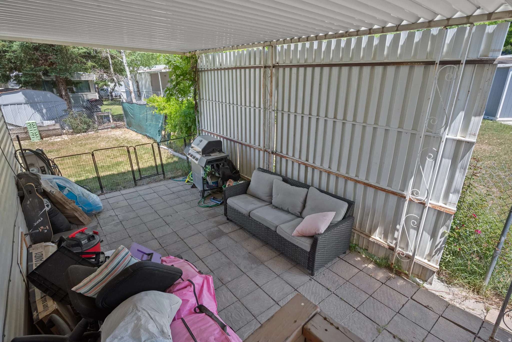Covered patio featuring paver flooring, a corrugated metal awning, and an open-air backyard beyond