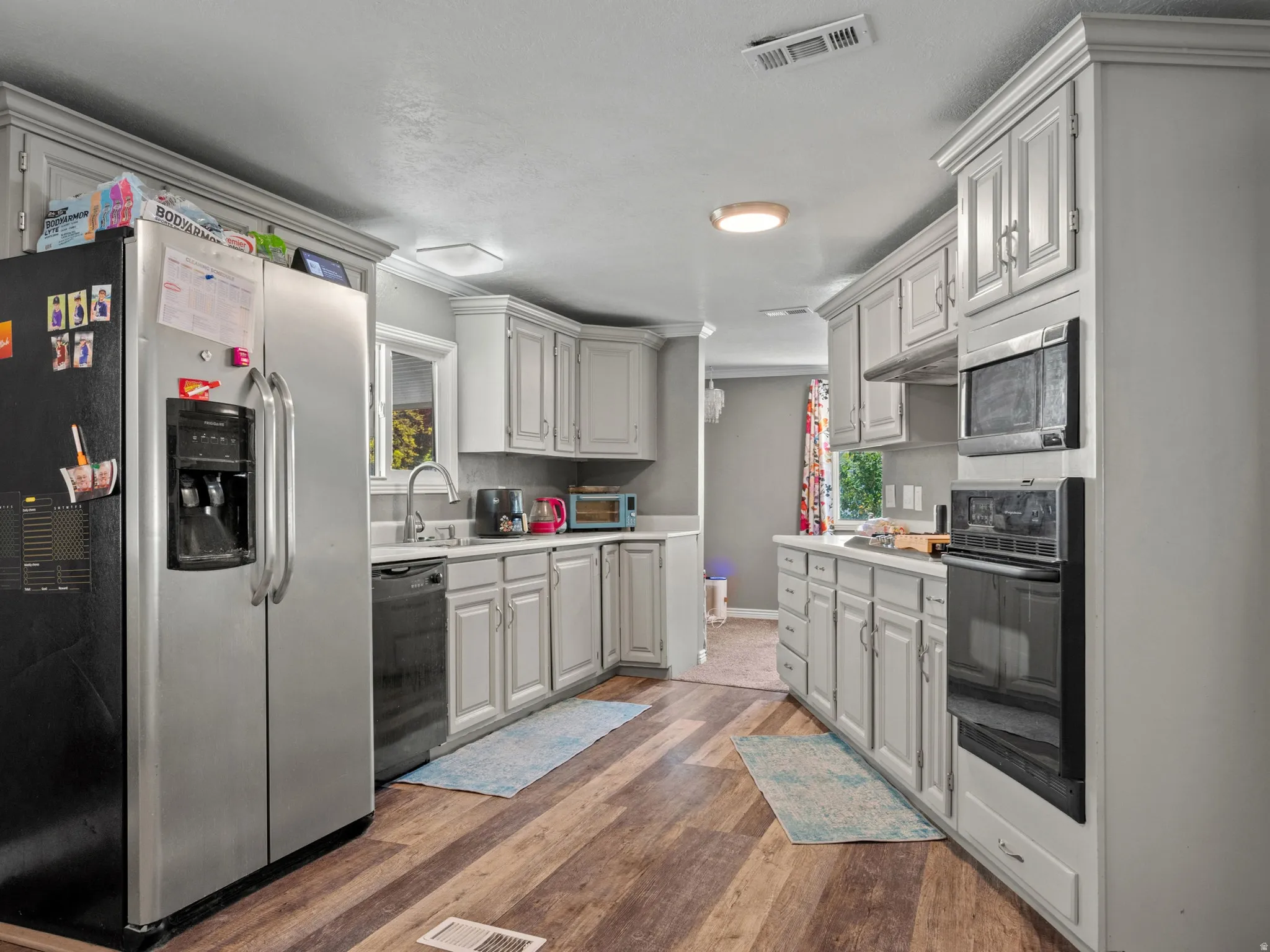 Kitchen featuring wood-finish flooring, light-toned cabinetry, stainless steel refrigerator, built-in microwave, and oven with a separate cooktop