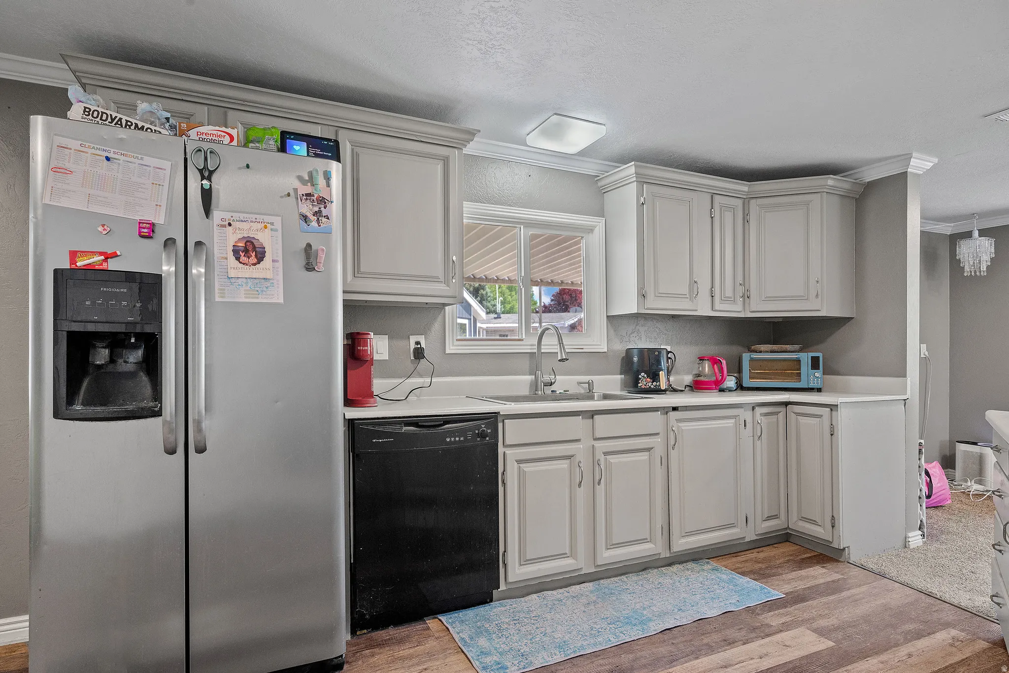 Kitchen featuring light gray cabinetry with crown molding, white countertops, stainless steel side-by-side refrigerator, black dishwasher, and wood-finish flooring