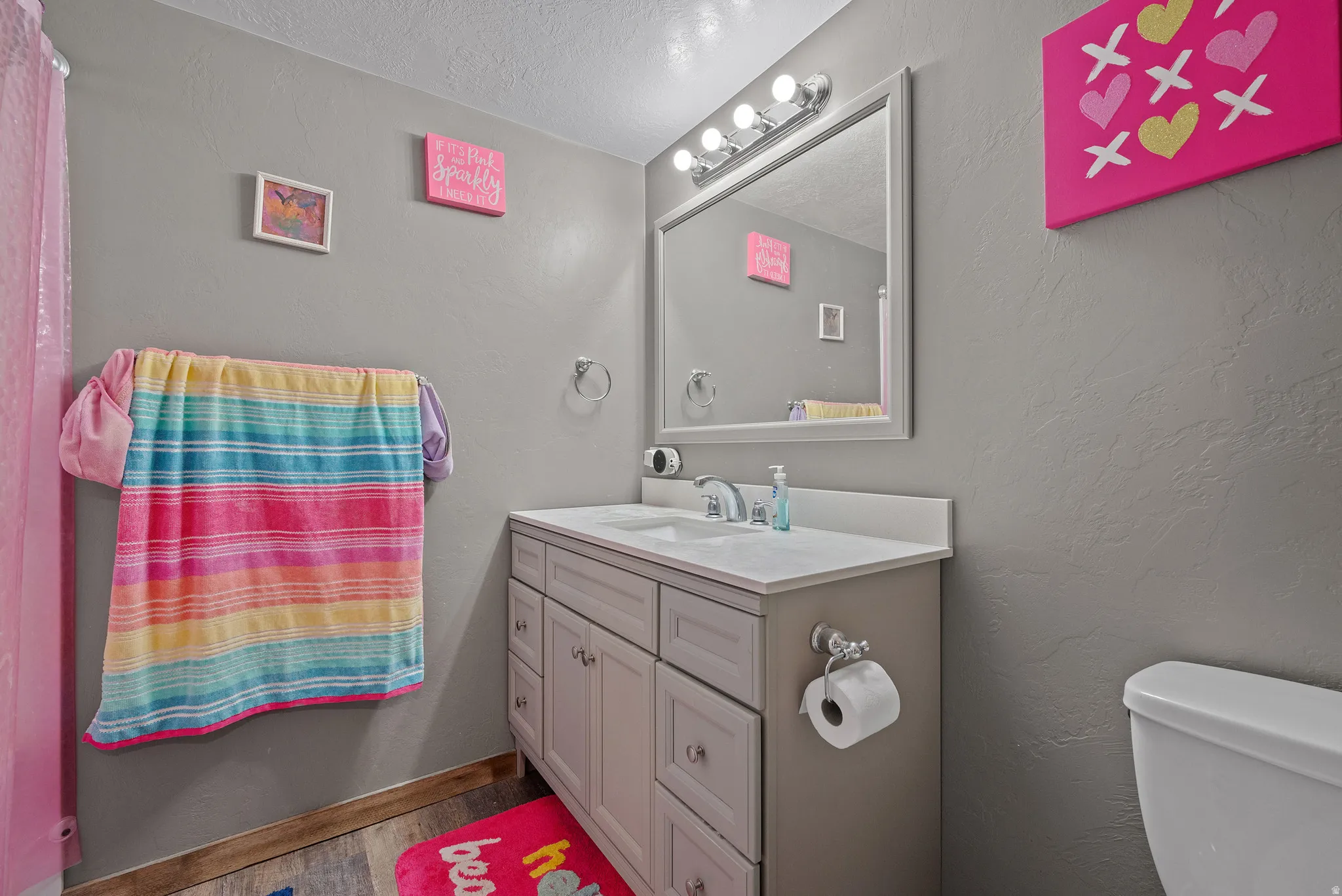 Bathroom featuring a light gray vanity with sink, an integrated white countertop, and a framed mirror with a four-bulb light fixture