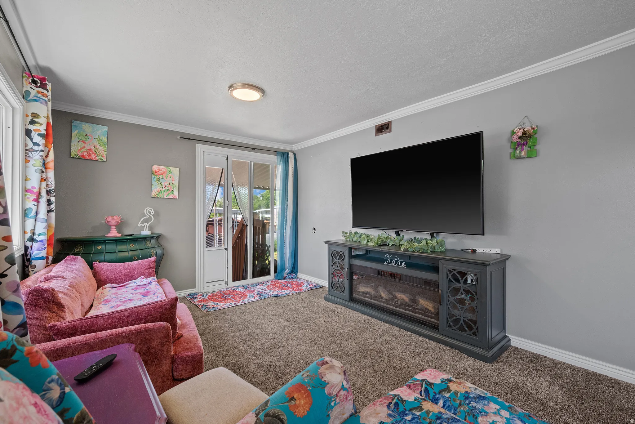 Carpeted living area featuring light gray walls, white crown molding, and a built-in media console with an integrated electric fireplace