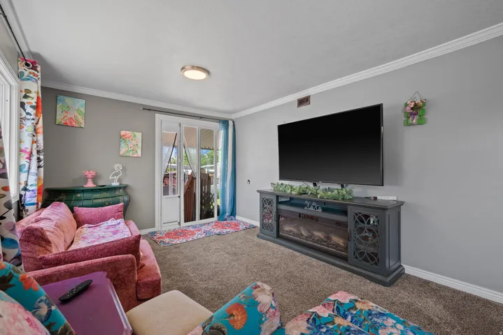 Carpeted living area featuring light gray walls, white crown molding, and a built-in media console with an integrated electric fireplace