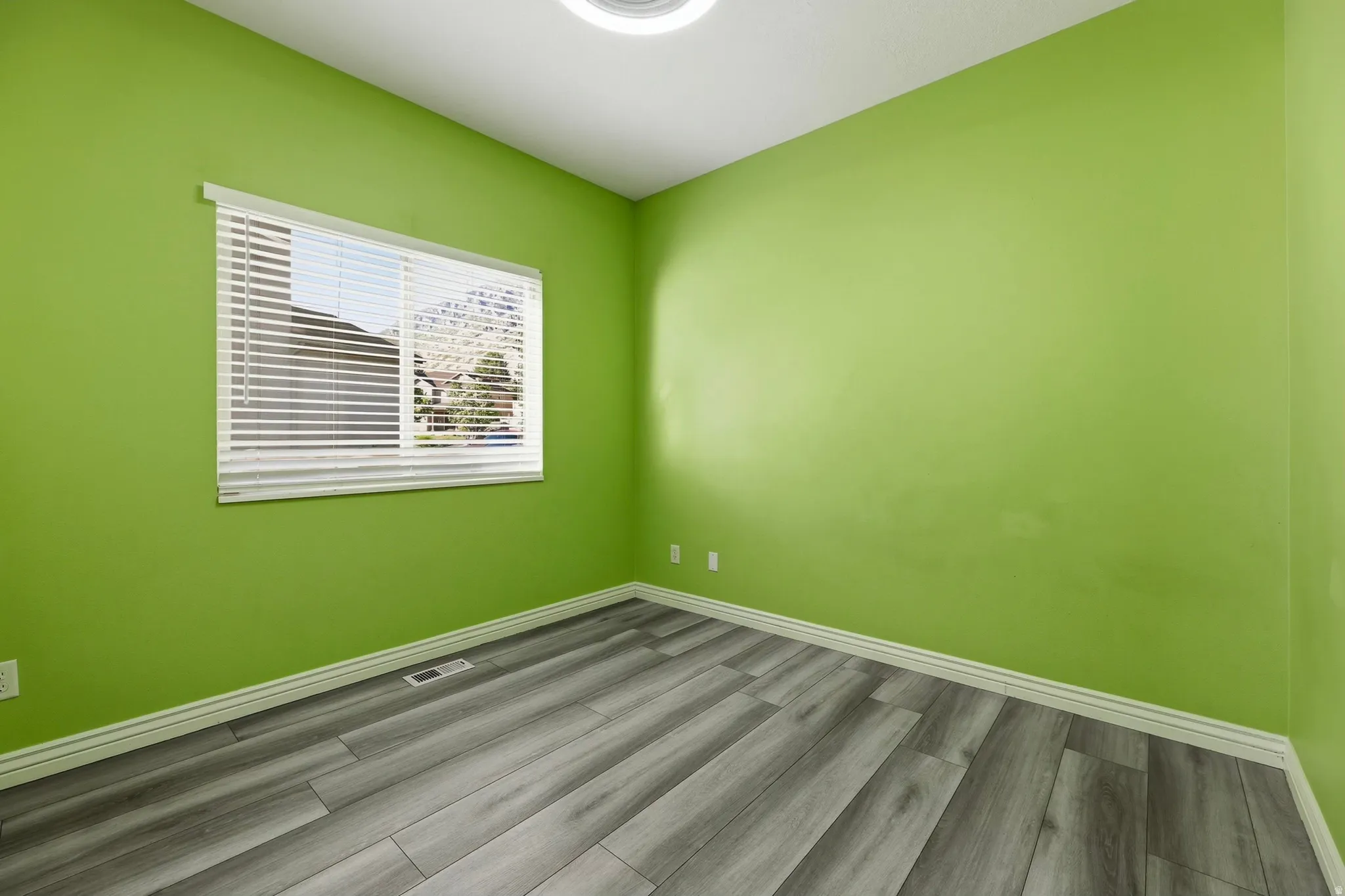 Room featuring wood-finish flooring, white baseboards, and a window with blinds