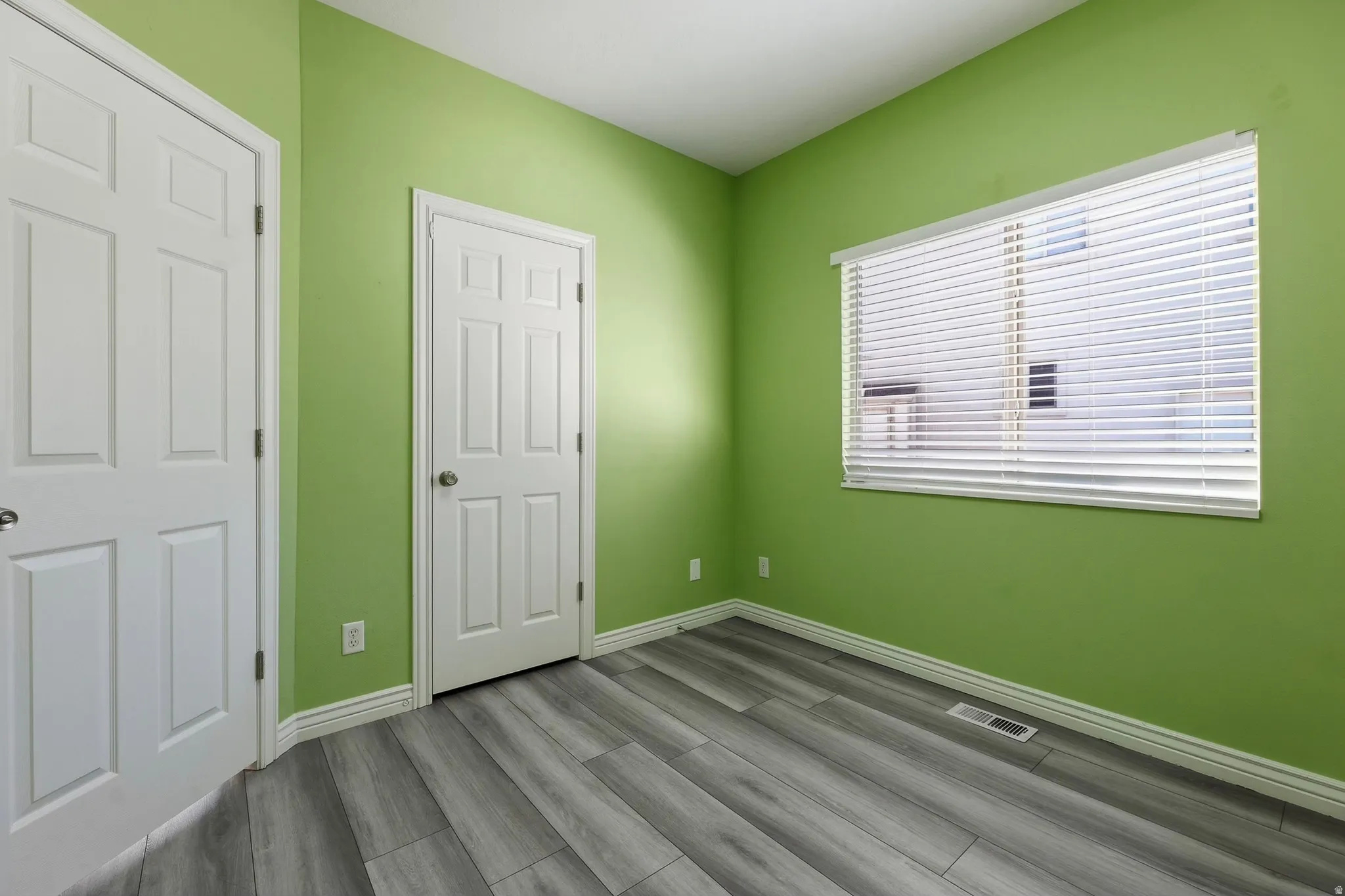 Room featuring wood-finish flooring, two white panel doors, and a window with horizontal blinds