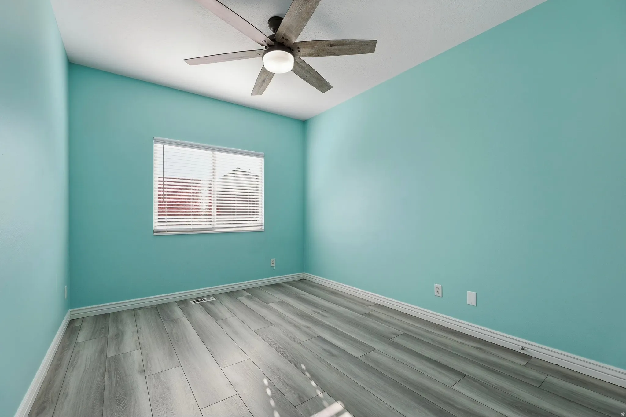 Room featuring wood-finish flooring, a ceiling fan with light fixture, and a window with horizontal blinds