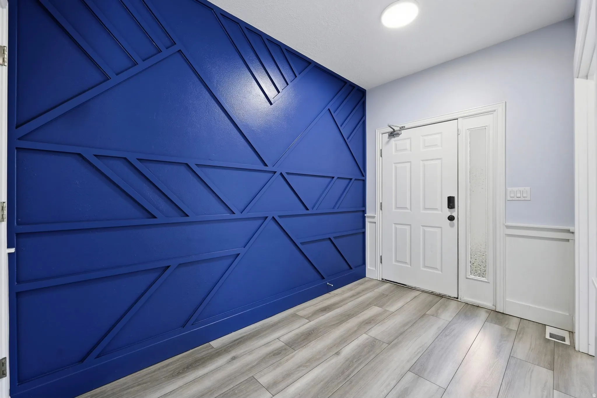 Entryway featuring a bold geometric accent wall, durable wood-finish flooring, a paneled entry door, a frosted glass sidelight, and recessed ceiling lighting