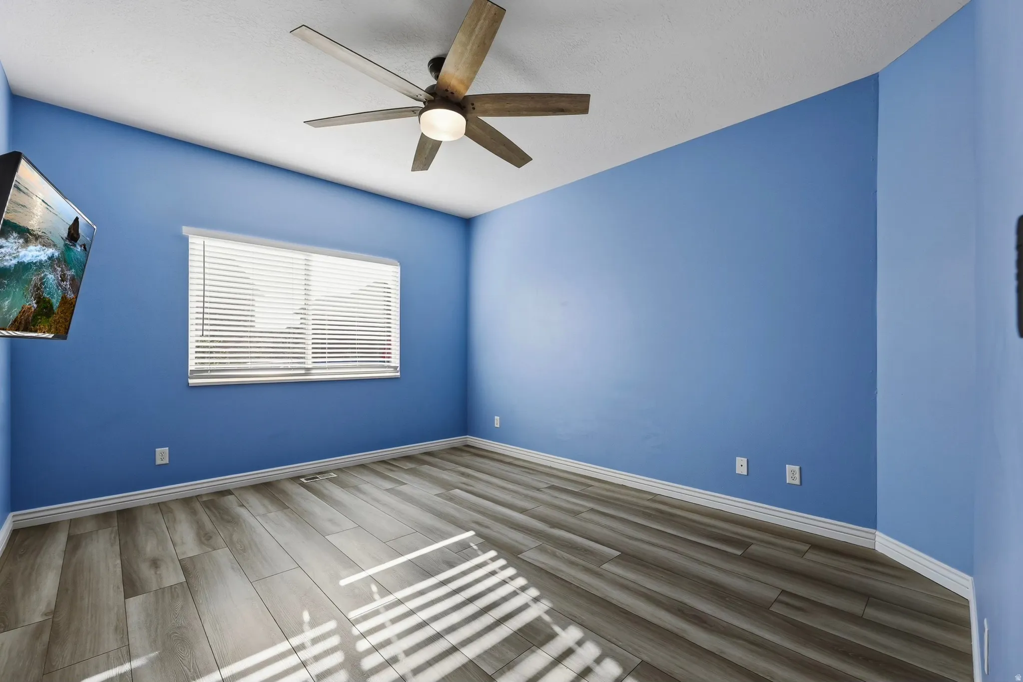 Room featuring wood-finish flooring, a ceiling fan with integrated lighting, and a window with horizontal blinds