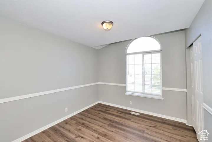 Room featuring a large arched window with horizontal blinds, wood-finish flooring, and a two-tone wall treatment with white chair rail molding