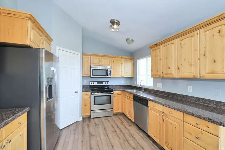 Kitchen featuring wood-finish cabinetry, stainless steel appliances, dark countertops, and wood-finish flooring