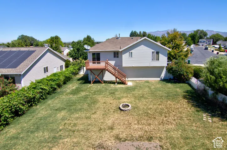 Expansive backyard featuring a deck with natural wood railing and stairs, a built-in fire pit, and partial fencing