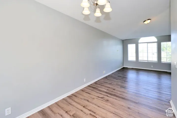 Spacious interior room featuring wood-finish flooring, vaulted ceiling, and multiple windows with an arched transom