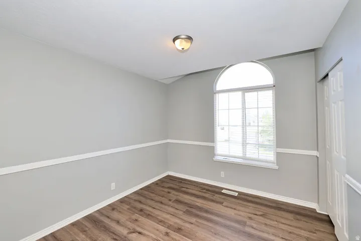 Room featuring a large arched window with horizontal blinds, wood-finish flooring, and a two-tone wall treatment with white chair rail molding