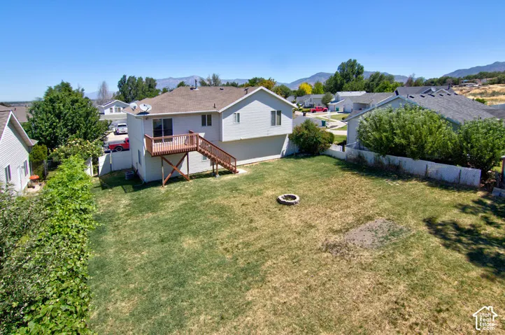 Spacious backyard featuring a fire pit, mature perimeter landscaping, and a two-story residence with a second-level wood deck and stairs