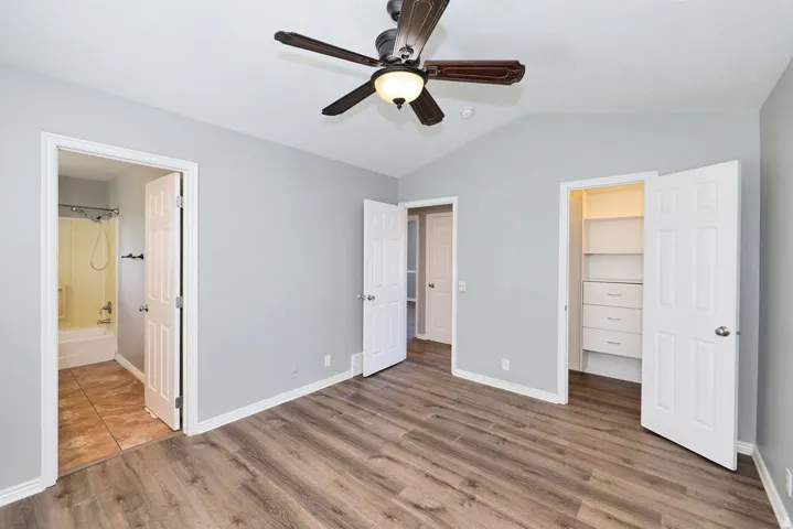 Vaulted ceilings with a ceiling fan light fixture, wood-finish flooring, white baseboards, and a built-in closet system featuring shelving and drawers
