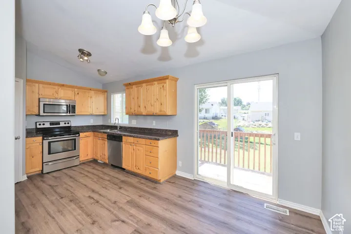 Kitchen featuring wood-finish flooring, light wood cabinetry, stainless steel appliances, and dark countertops