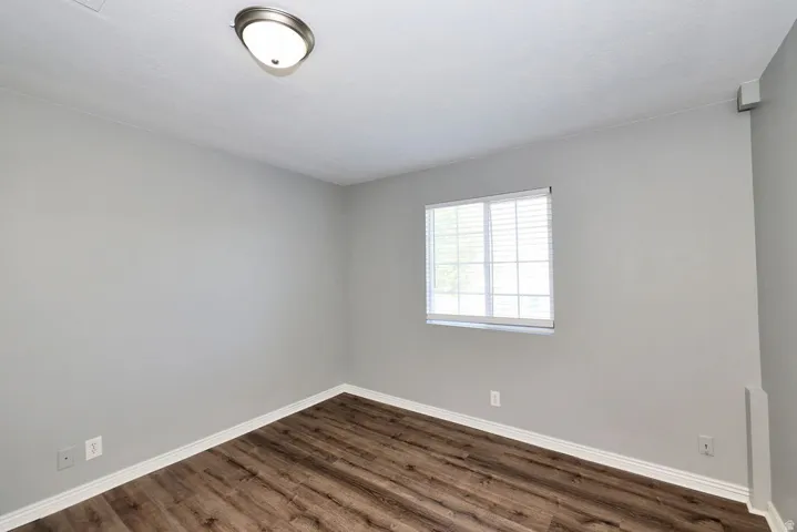 Spacious room featuring wood-finish flooring, light grey walls, and a window with blinds