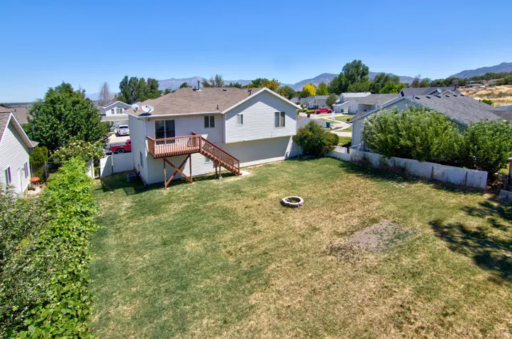 Spacious backyard featuring a fire pit, mature perimeter landscaping, and a two-story residence with a second-level wood deck and stairs