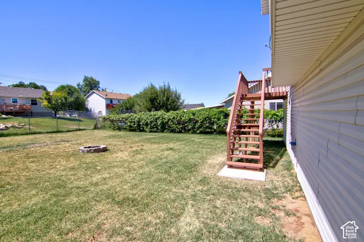 Expansive backyard featuring a wood deck with stairs, a stone fire pit, and mature perimeter landscaping