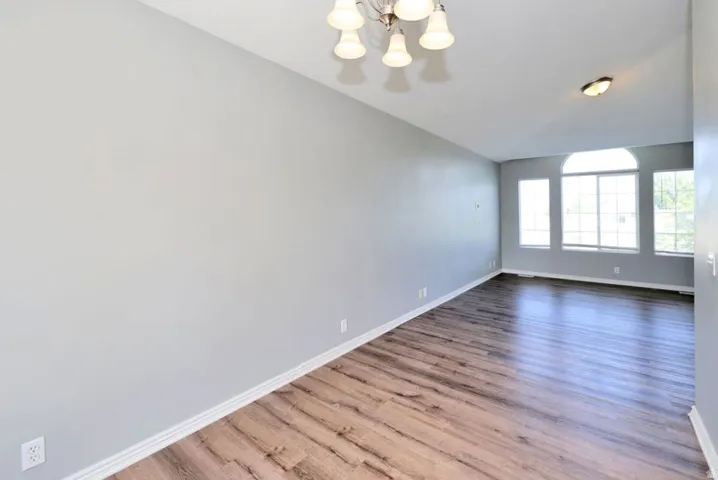 Spacious interior room featuring wood-finish flooring, vaulted ceiling, and multiple windows with an arched transom
