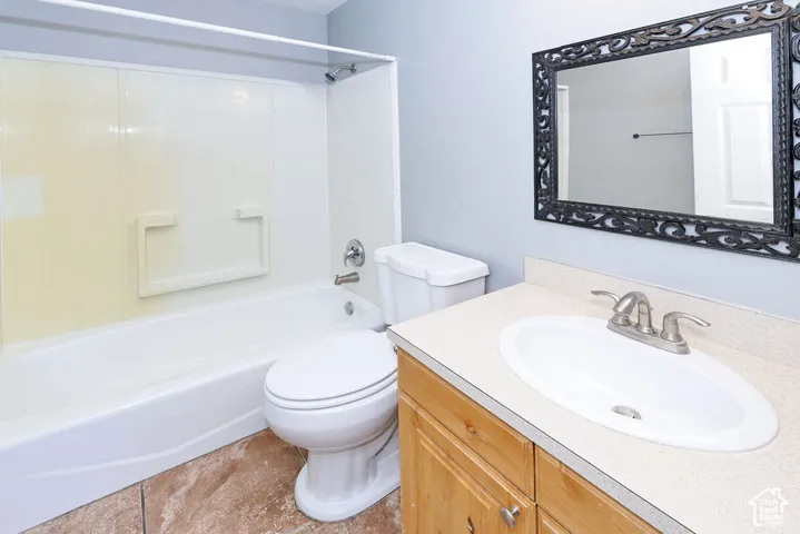 Full bathroom featuring a white bathtub/shower combination, a vanity with a light-colored countertop and an integrated sink, a wood-finish cabinet, and a decorative framed mirror