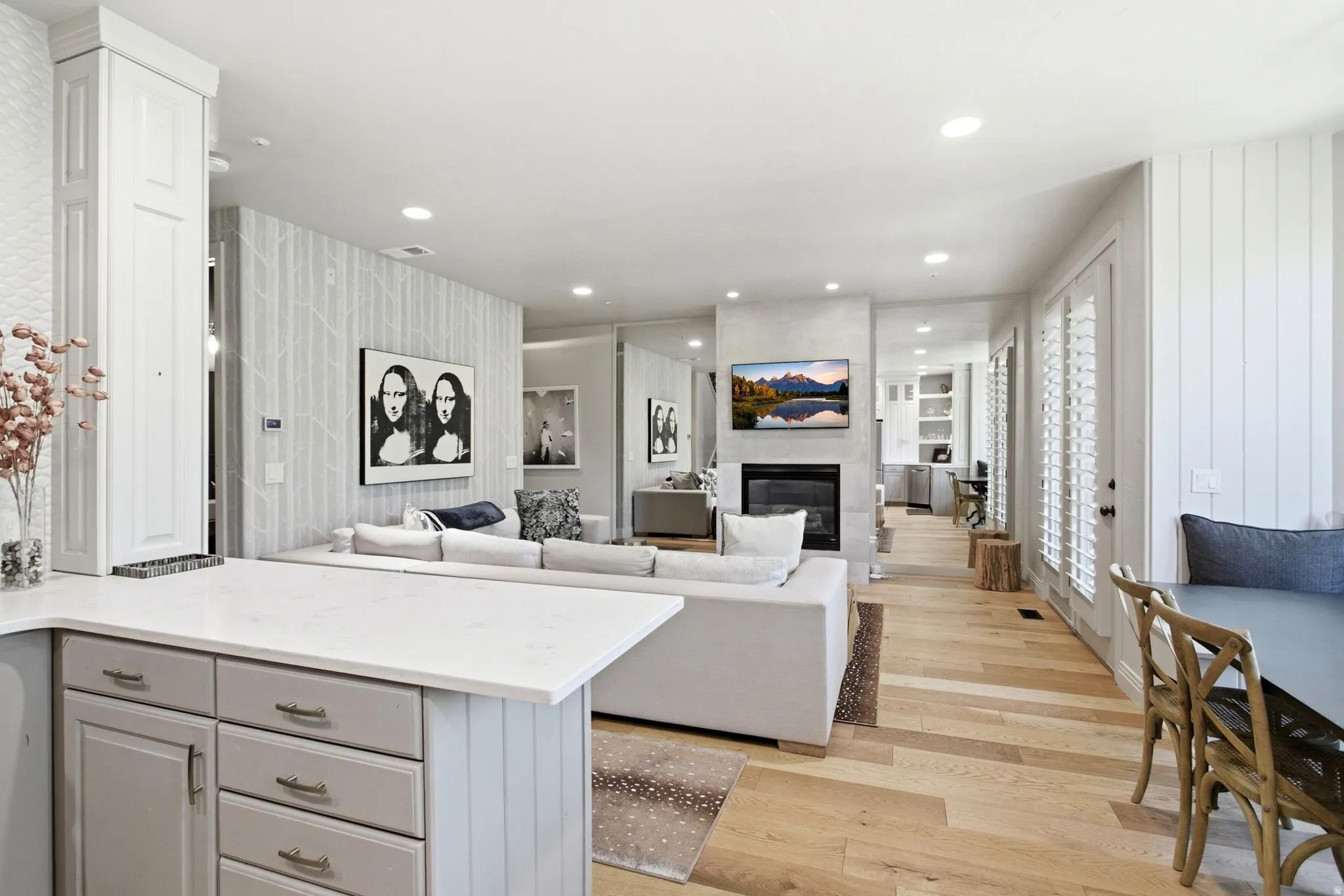 Open-concept living area featuring light wood-finish flooring, a contemporary fireplace with a mounted television, and recessed ceiling lighting