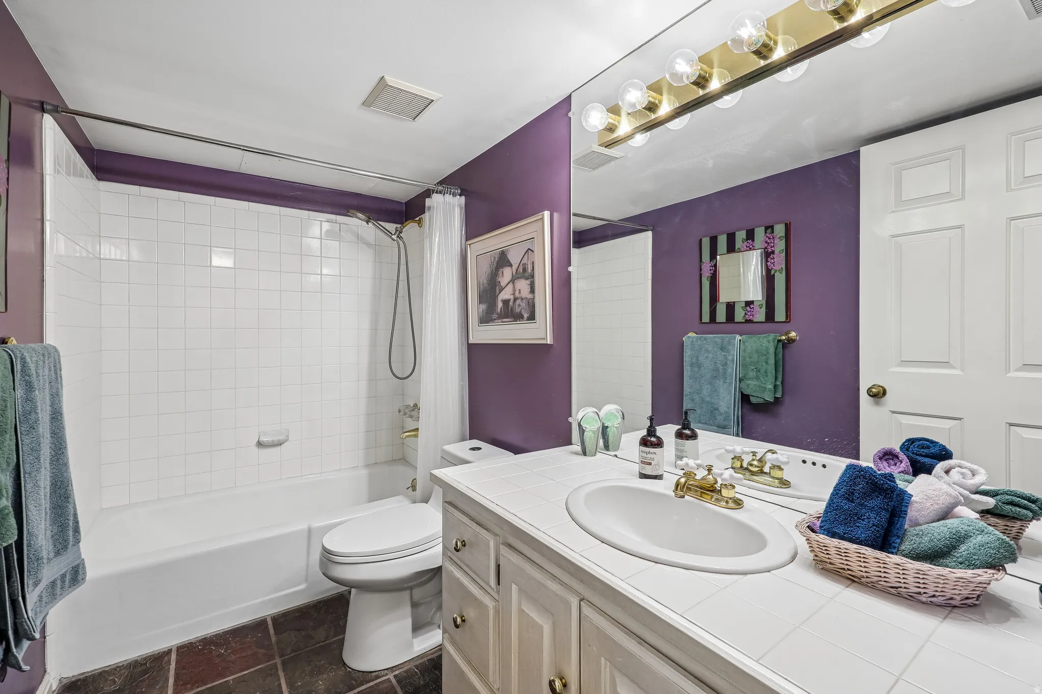 Bathroom vanity featuring an oval undermount sink with a gold-tone faucet, set into a white tile countertop