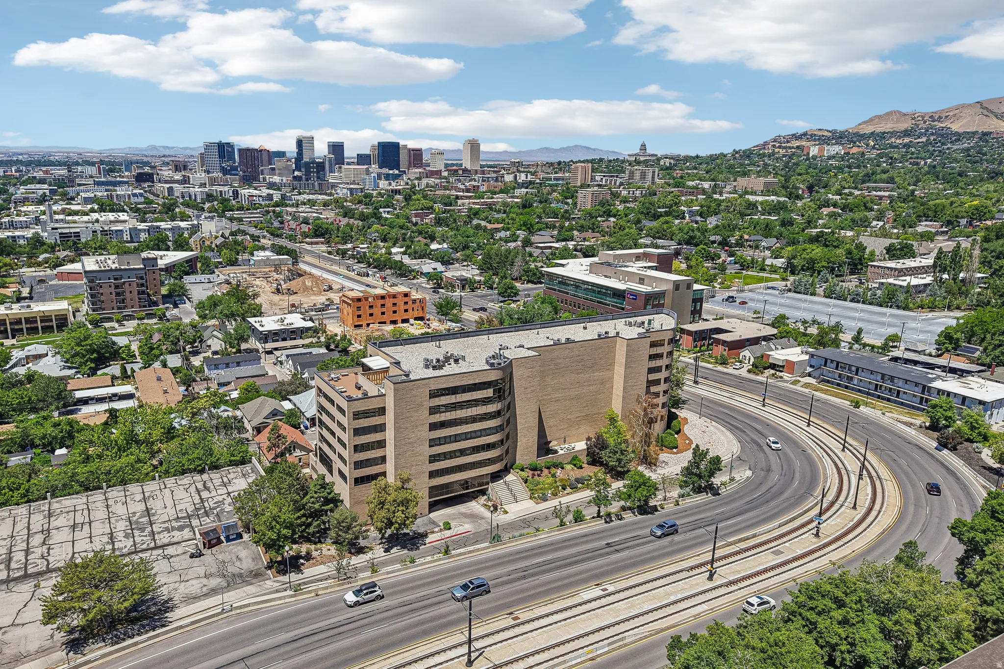 Urban landscape featuring a prominent commercial building with a curved facade, multi-lane roadway, and light rail tracks