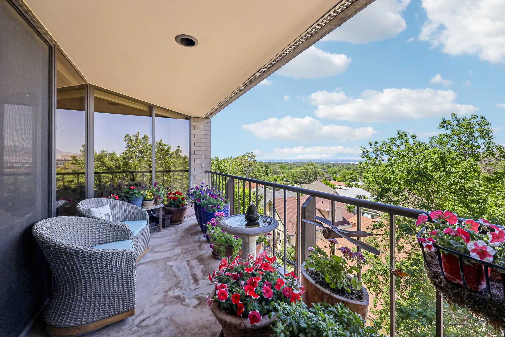 Expansive outdoor balcony featuring a stone tile floor, black wrought iron railing, and large floor-to-ceiling windows