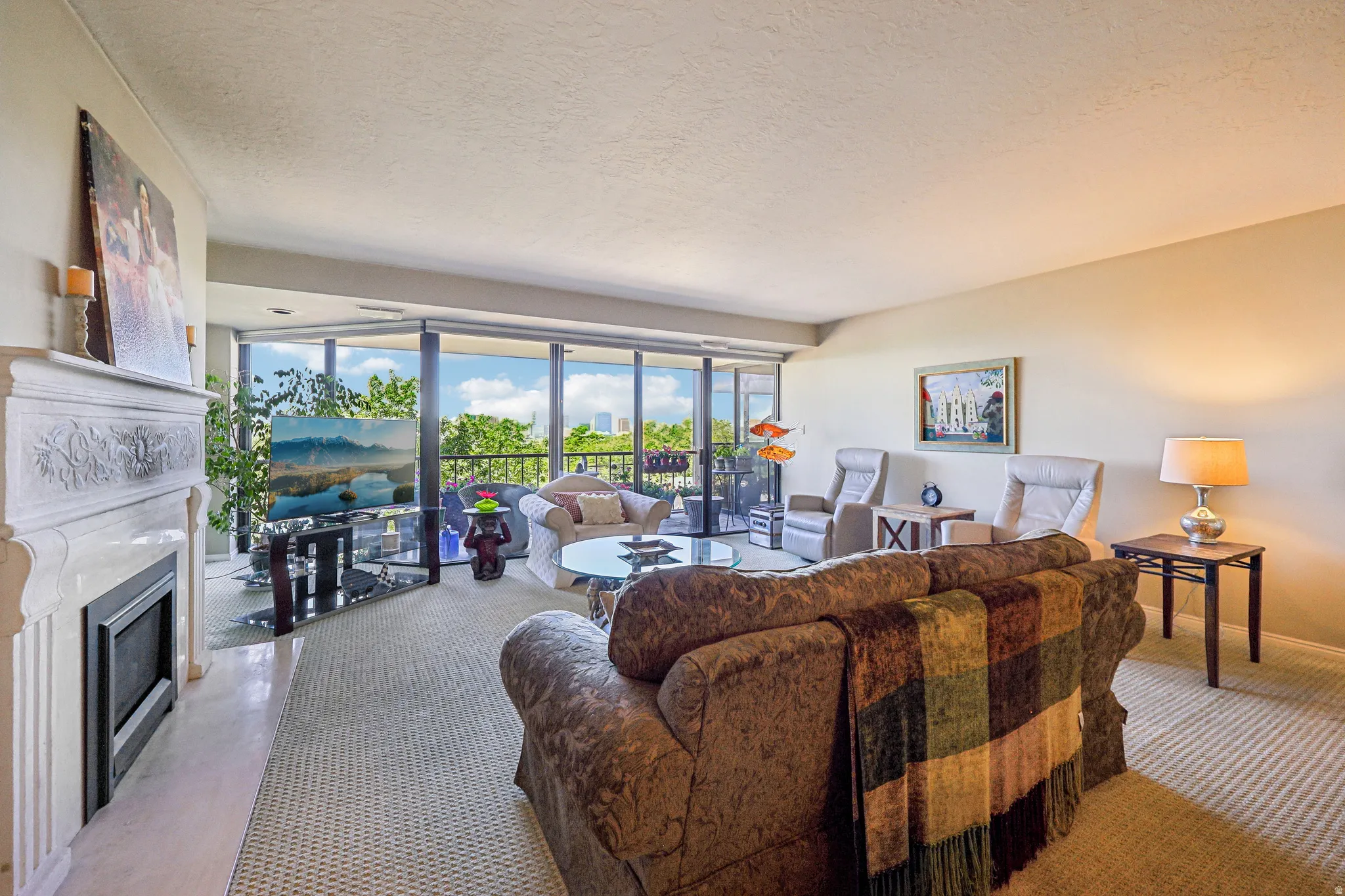 Spacious living area featuring a built-in fireplace with an ornate mantel, floor-to-ceiling glass paneling, and access to an outdoor balcony